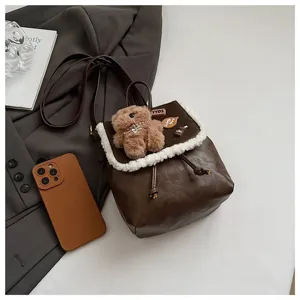Detail shot of retro brown leather backpack with fluffy white trim and cute teddy bear charm.