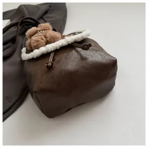 Detail shot of the brown faux leather mini backpack featuring white plush trim and cute bear charm.