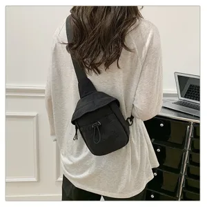 Close-up detail shot of the casual black cross-body chest bag worn outdoors by a model.