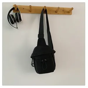Detail shot of the minimalist black crossbody chest bag hanging neatly on a wooden wall hook.