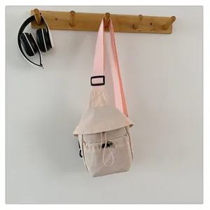Casual minimalist sling chest bag detail showcasing the soft pink strap and beige canvas fabric.