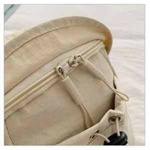 Close-up detail shot of beige nylon crossbody chest bag showing zipper and hardware accessories.