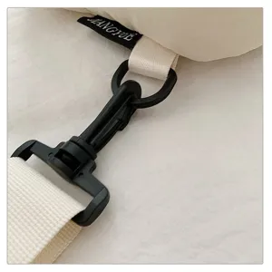 Close-up detail of the crossbody bag strap buckle and metal hardware hook, minimalist design.