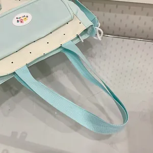 Close-up detail of the light green canvas shoulder bag, featuring cute polka dots and straps.