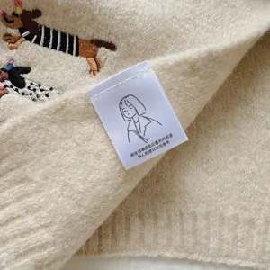 Close-up detail of beige knitted scarf featuring cute dachshund embroidery and label.