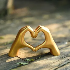 Close up of golden heart hand gesture sculpture ornament on rustic wooden background.