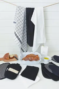 Vue détaillée du set textile de cuisine avec gants de four noirs, blancs et torchons suspendus.