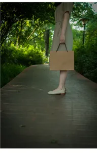 Outdoor detail shot of minimalist brown kraft paper gift bag with black handles on path.