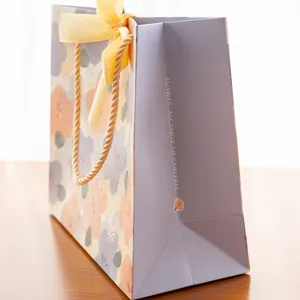 Sac cadeau en papier à fleurs fraîches avec ruban nœud jaune et design élégant pour fêtes.