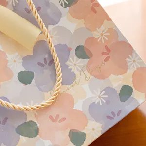Sac cadeau floral aquarelle frais avec texte doré et poignée ruban pour emballage chic.
