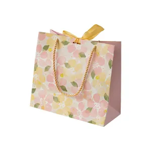 Sac cadeau en papier à fleurs avec poignée dorée et joli ruban pour emballage élégant.
