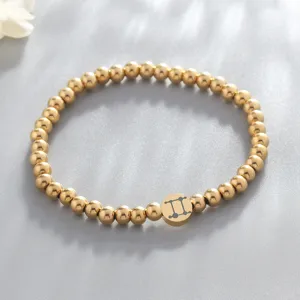 Closeup of the gold beaded bracelet featuring a Gemini zodiac sign charm on gray background.