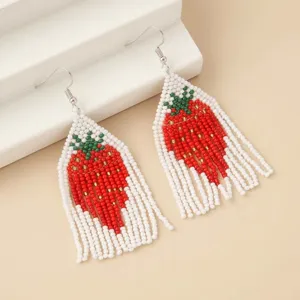 Detail shot of handmade strawberry seed bead fringe earrings with green top and white base.