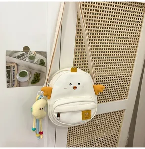 Cute cartoon chick crossbody bag for girls, white canvas shoulder bag with plush pendant.