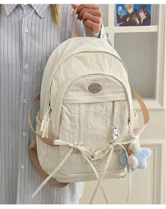 Detail view of cute nylon casual student backpack with ribbons and plush pendant in beige.