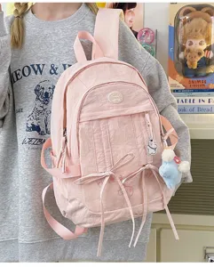 Detailed view of cute pink nylon school backpack with ribbon bows and bear pendant style.