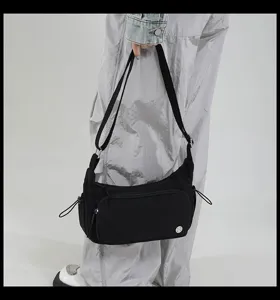 Dettaglio borsa a tracolla in nylon nero con tasca frontale con zip e logo metallico.
