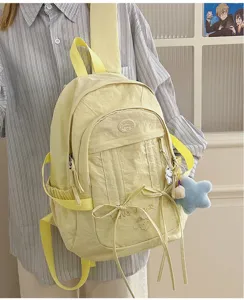 Detail view of casual nylon school backpack in light yellow with cute pendants and front pockets.