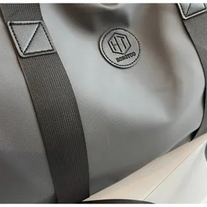 Détail de grand sac de voyage, tissu gris durable avec sangles noires et logo.