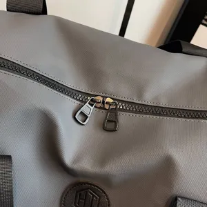 Détail de sac de voyage gris avec tissu durable, double fermeture éclair et patch en cuir.
