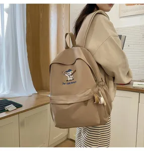 Details of beige backpack with cute baseball dog embroidery and charm pendant for daily use.