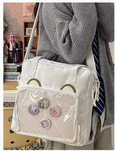 White canvas ita bag with clear front window and cute pin badges for anime fans daily use.