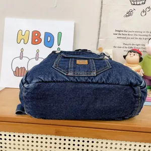 Denim backpack detail view showing the front pocket, metal buttons, and vintage denim fabric texture.