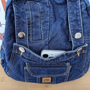 Close-up detail of denim backpack front pocket and metal button design, textured fabric.