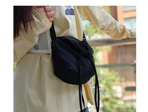 Detail view displaying the black nylon drawstring crossbody dumpling bag worn by model outdoors.