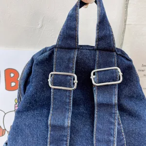 Detailed view of dark blue denim backpack featuring adjustable metal buckles and sturdy top handle.