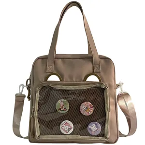 Detail view of a cute khaki ita bag with transparent window, pins and crossbody strap.