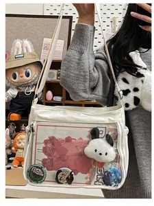 White transparent ita bag detail showing clear window, plush charm, and custom pin badges inside.