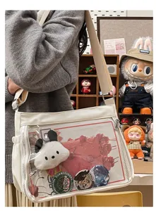 Detail shot of white canvas crossbody itabag with clear window, badges, and cute plushie charm.