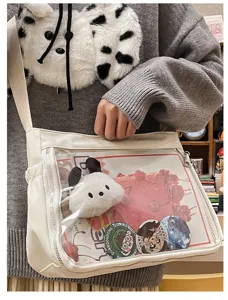 Detailed view of white transparent ita bag with cute badges and plush pendant, front clear pocket.