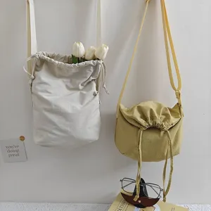 Detail view of casual nylon drawstring messenger dumpling bags hanging on white wall with props.
