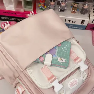 Nahtaufnahme des rosa-weißen Studentenrucksacks mit Vordertaschen, Schnallen und süßem Tisch.