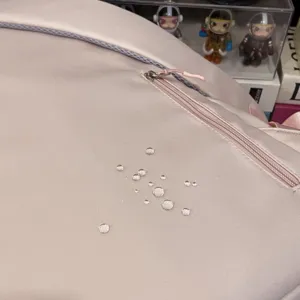 Detailansicht des rosa wasserdichten Schulrucksack-Stoffes mit Wassertropfen-Abperleffekt.