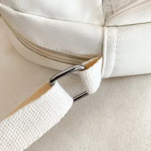 Gros plan detaille de la sangle de sac en toile blanche, boucle carree et fermeture eclair.