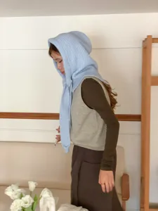 Detail shot of light blue knitted balaclava hood scarf, soft texture worn by model in room.