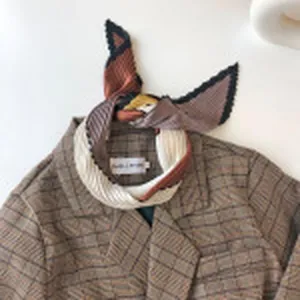 Gedetailleerd overzicht van een geometrische color-block zijden sjaal op geruite blazer.
