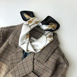 Detailansicht eines Luxus-Seidenschals mit Vintage-Kutschmuster auf kariertem Blazer.