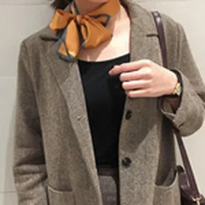 Close-up detail shot of a stylish orange silk neck scarf tied as a bow with a blazer.