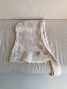 Detailed view of beige knit balaclava hood scarf, showing fine texture, buttons and brand tag.