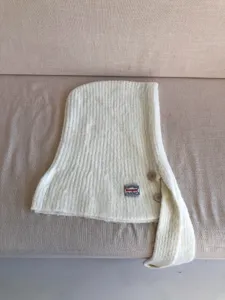 Close-up detail of knitted balaclava hood scarf with button and woven label texture.