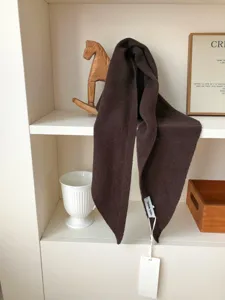 Primer plano de un pañuelo triangular de lana marrón oscuro con textura suave y diseño cálido.