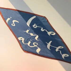 Pleated diamond scarf detail showcasing soft fabric texture and artistic letter print.