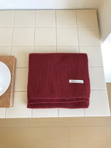 Primer plano de la textura de la bufanda de punto burdeos, doblada ordenadamente sobre azulejos blancos.