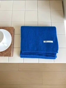 Primer plano detallado de una cómoda bufanda de punto azul doblada sobre azulejos blancos.