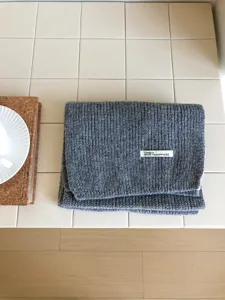 Vista detallada de bufanda de punto gris con textura de lana suave y etiqueta de marca.