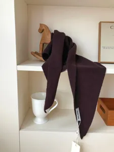 Detalle en primer plano de bufanda triangular de lana marrón en estante de madera.